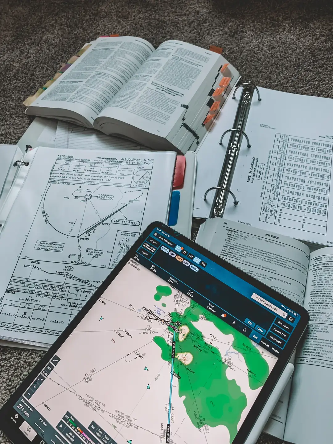 A pile of FAA pilot handbooks, sectional charts, and study materials scattered on the floor