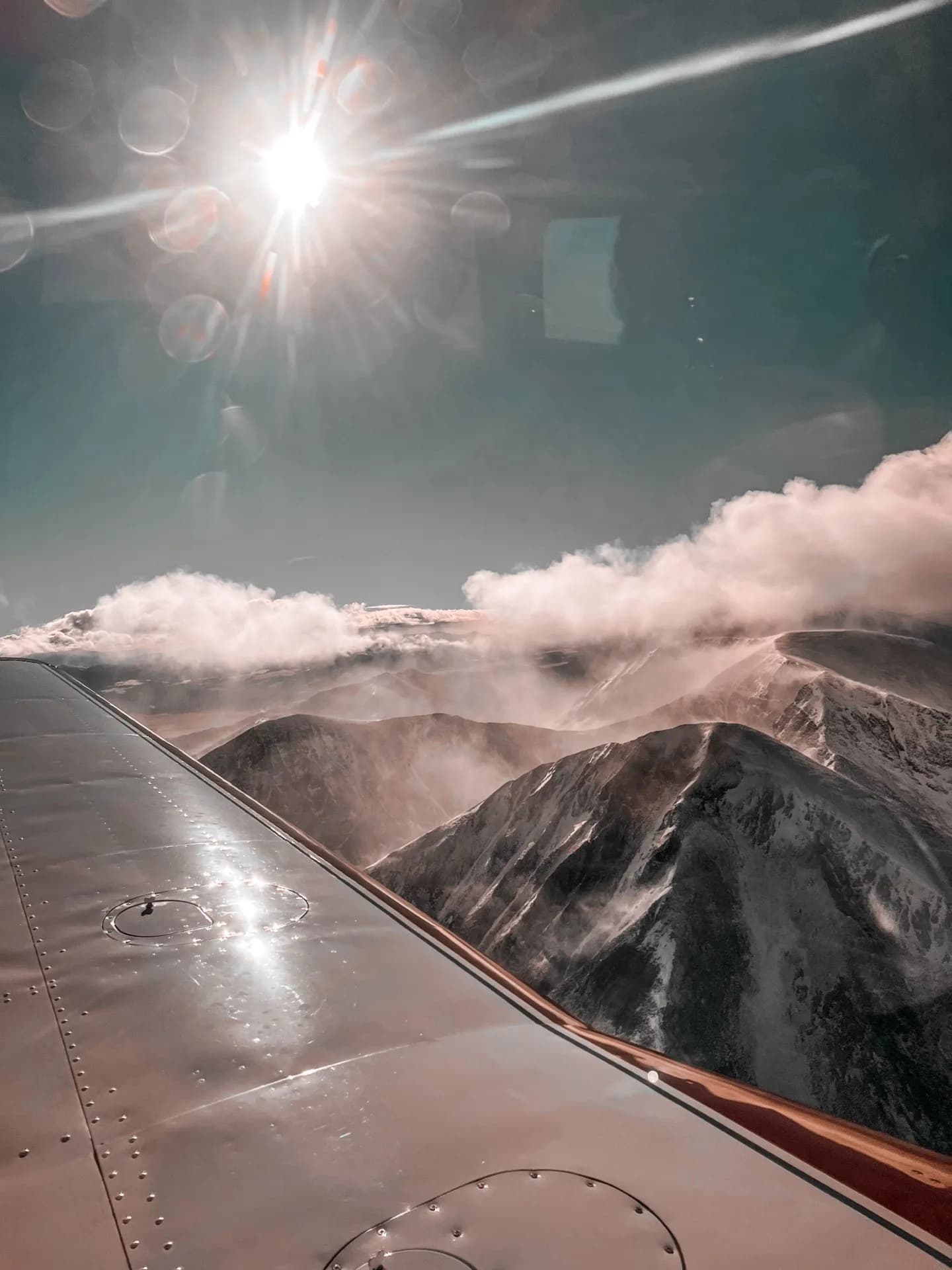 Sunlight above clouds and a mountain range, seen from an aircraft